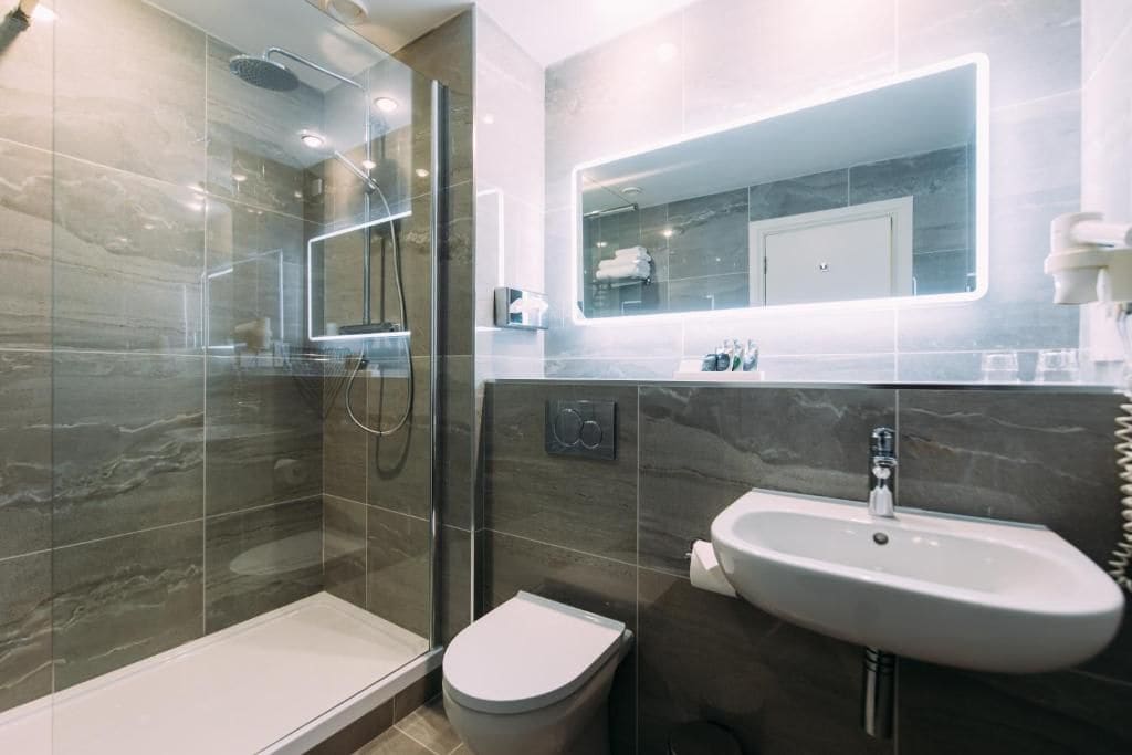 A modern bathroom with a glass-enclosed shower, a toilet, and a sink with a mirror above.
