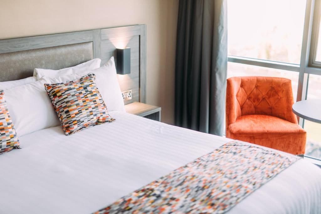 Une chambre d’hôtel avec un lit, une table de chevet, une lampe, une chaise et une fenêtre.
