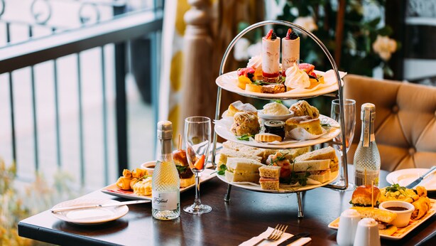 A three-tiered dessert stand with various pastries and a bottle of champagne on a table in a dining area. - Armagh City Hotel (Armagh)