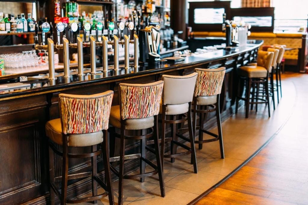 A bar area with multiple stools and a bar counter with a variety of bottles and glasses.