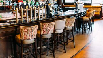 A bar area with multiple stools and a bar counter with a variety of bottles and glasses.