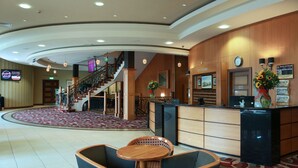 A hotel lobby with a reception desk, seating area, staircase, and a clock on the wall. - Armagh City Hotel (Armagh)