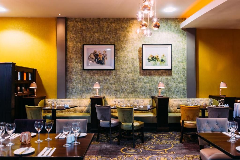 A restaurant with a sofa and dining tables, framed artwork on the wall, and a patterned carpet.
