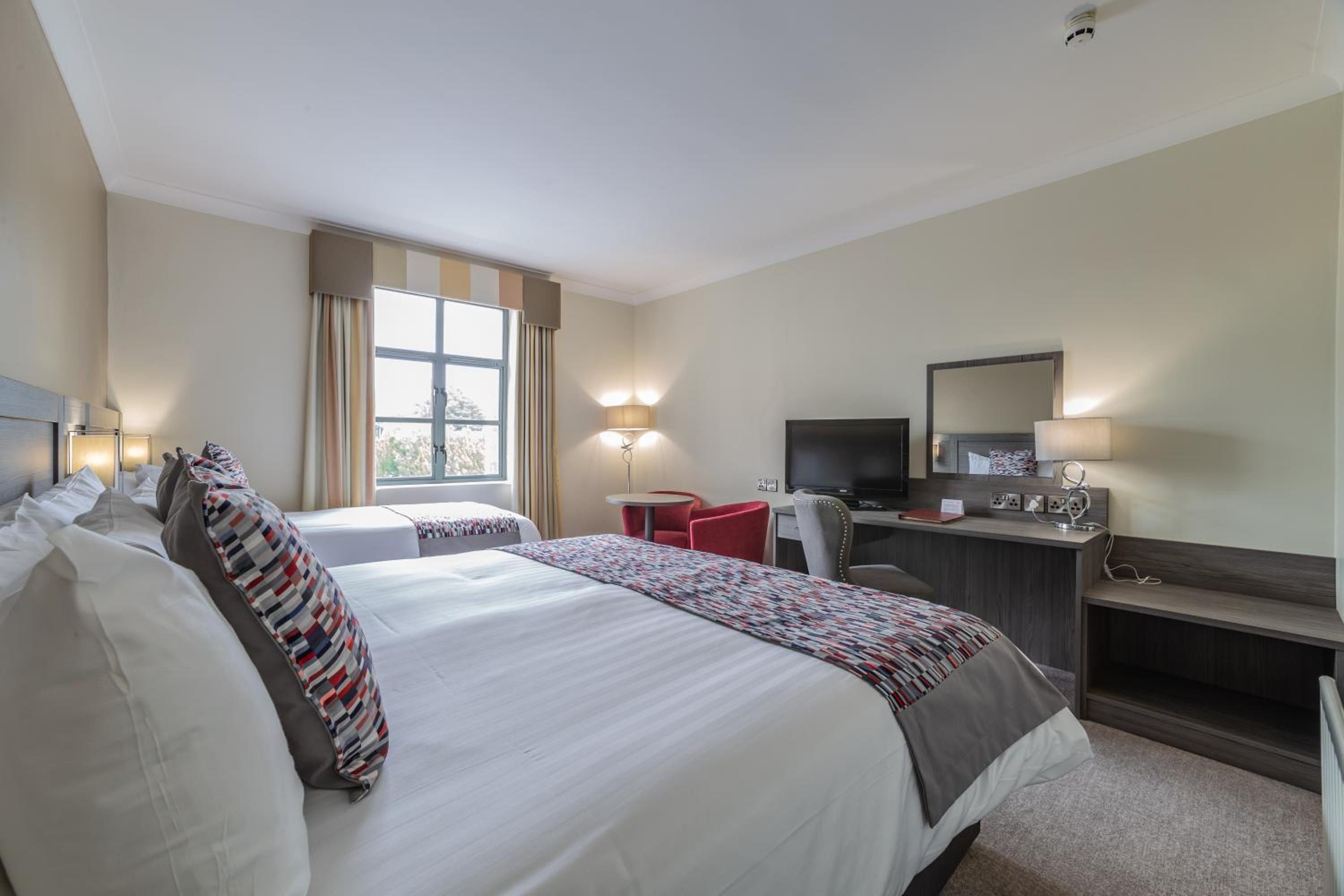 Habitación de hotel con una cama grande, un escritorio con computadora, un televisor y una ventana con cortinas.