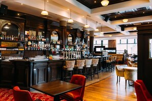 Un espace bar doté d’un comptoir en bois, de différents types de sièges, notamment des tabourets et des tables, ainsi que d’une variété de bouteilles et de verres exposés sur des étagères.