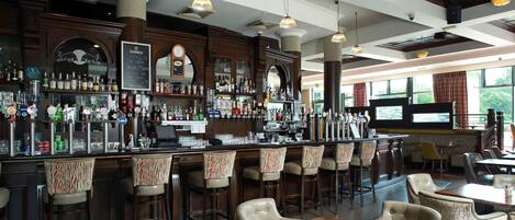A bar area with multiple stools, a bar counter with various bottles, and a clock on the wall.