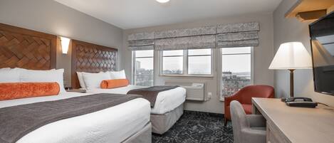 Een hotelkamer met twee bedden, een bureau, een stoel en een groot raam met uitzicht op de stad.