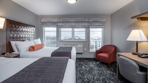 Habitación de hotel con dos camas, un escritorio, una silla, un ventanal y una alfombra estampada.