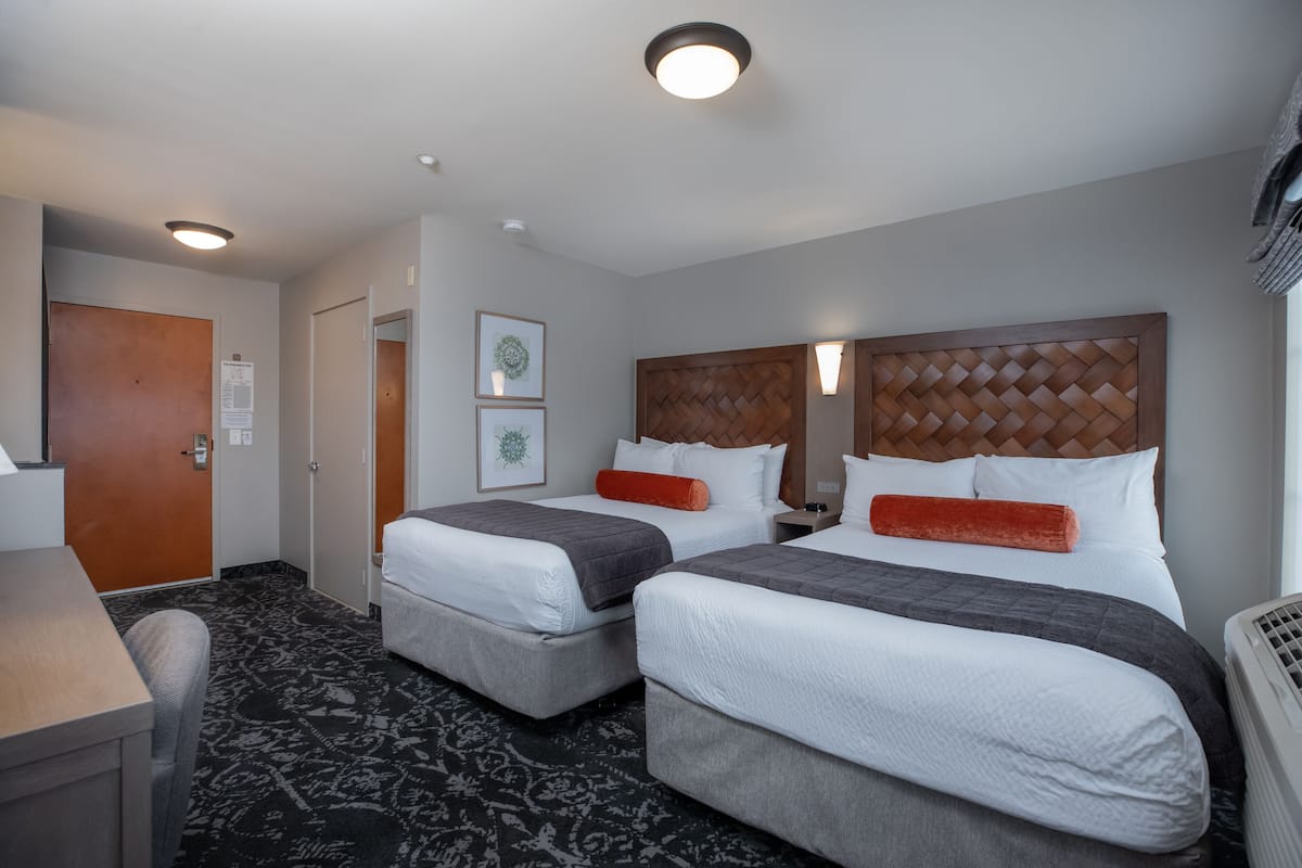 A hotel room with two beds, a desk, and a chair.