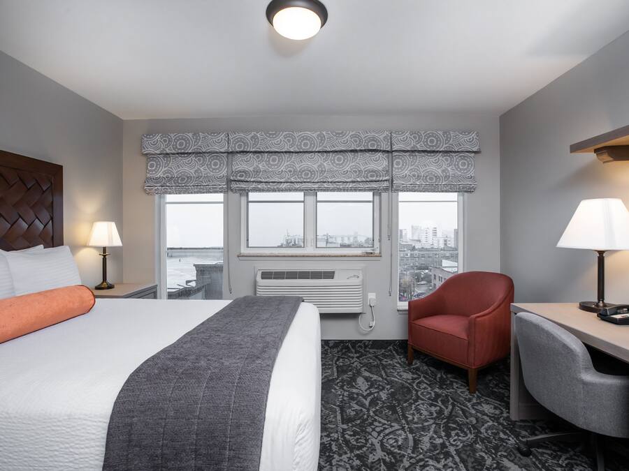 A hotel room with a bed, a desk, a chair, a window with a view, and a patterned carpet.
