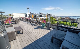 A deck with outdoor furniture, potted plants, and a view of the city skyline including a tower.