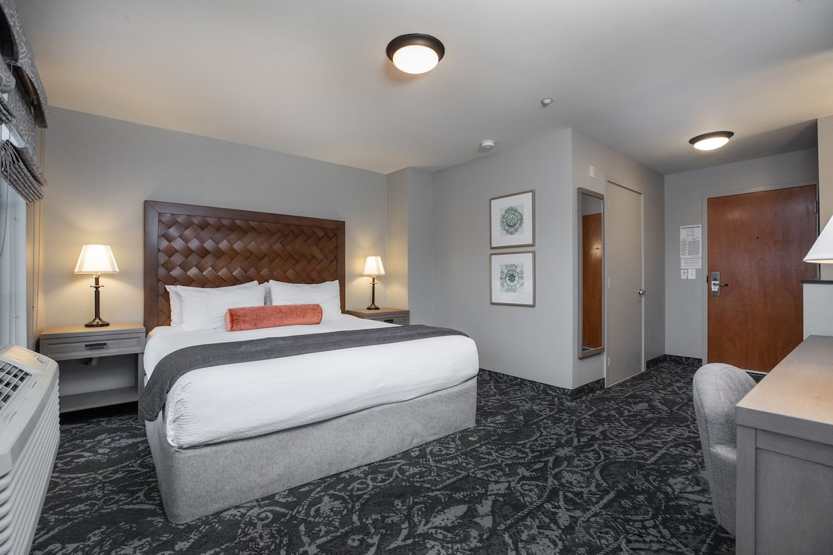 A hotel room with a large bed, two bedside lamps, a desk, and a chair.