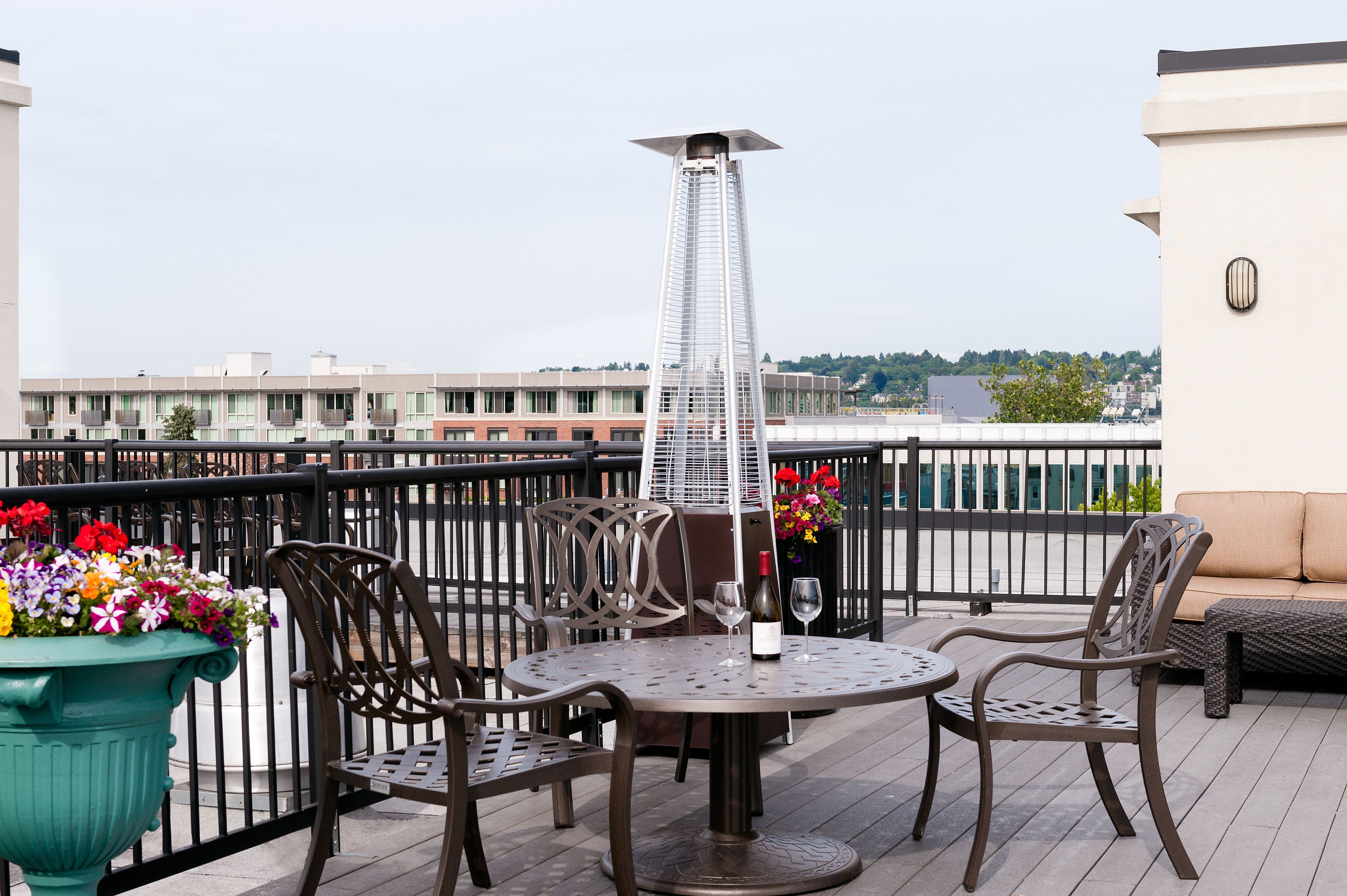 A rooftop terrace with a round table, chairs, a decorative metal sculpture, and a flower planter.