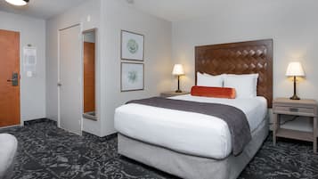 Una camera d'albergo con un letto grande, due comodini con lampade, una porta e un pavimento rivestito di moquette.