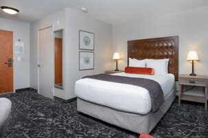 A hotel room with a large bed, two bedside tables with lamps, a door, and a carpeted floor.