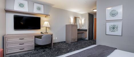 Habitación de hotel con cama, escritorio, silla, televisor, armario y obras de arte en las paredes.