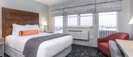 Habitación de hotel con una cama grande, una silla roja, un escritorio y una ventana con un adornado cortinero.