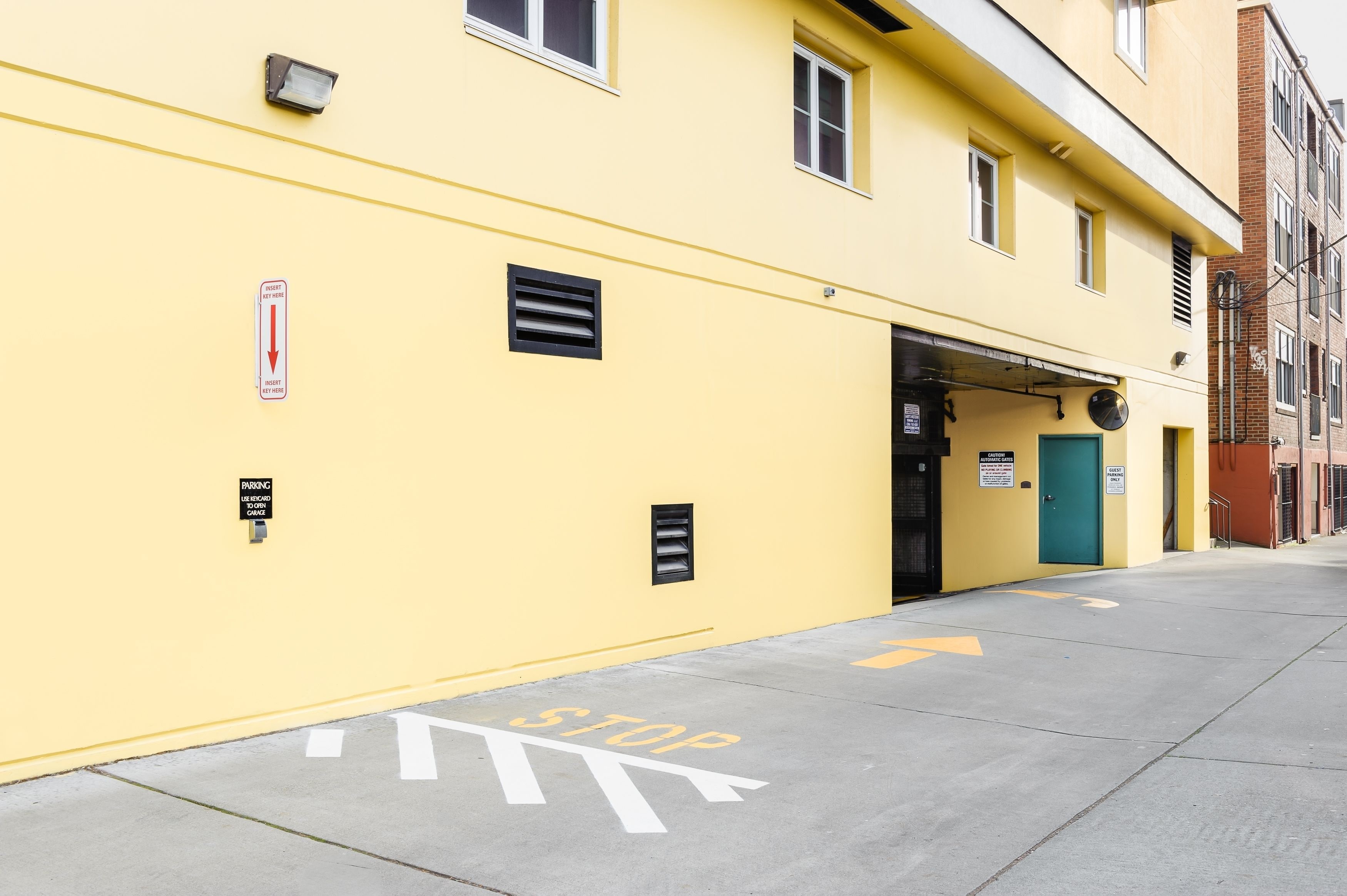 A yellow building with a garage door, a stop sign on the pavement, and a parking sign.