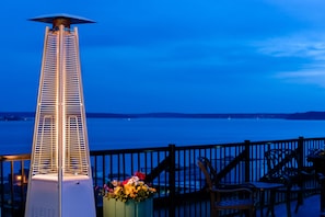 A tall, white heater with a metal grill, a wooden fence, and a view of the water. - Mediterranean Inn (Seattle)
