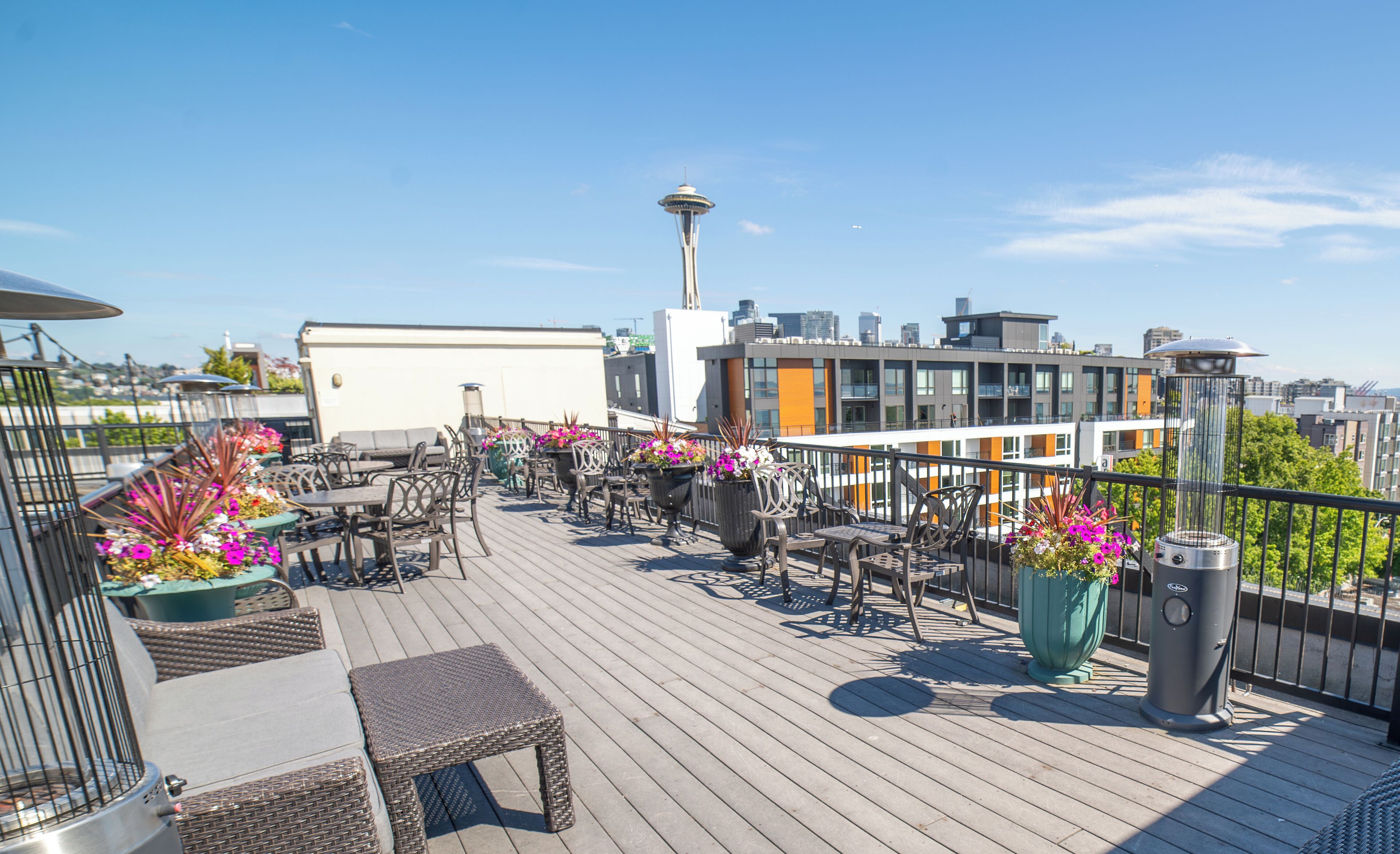 A rooftop terrace with outdoor seating, potted plants, and a view of the Space Needle.