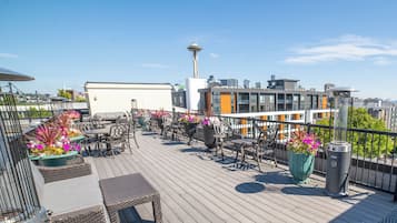 A rooftop terrace with outdoor seating, potted plants, and a view of the Space Needle.