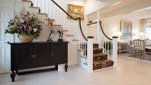 A staircase with a wooden handrail and white walls, leading to a living area with a sofa and a lamp. - The Wauwinet (Nantucket)