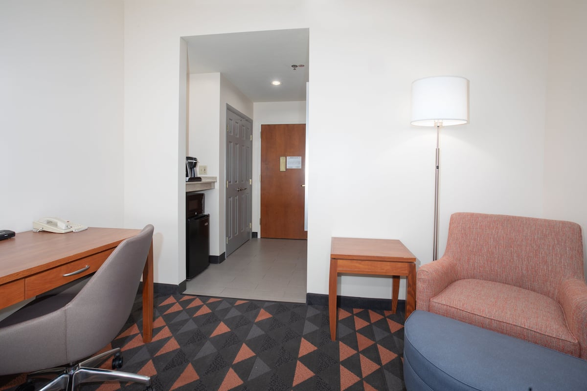 Una habitación de hotel con un escritorio de madera, una silla azul, una mesita pequeña y una lámpara.