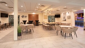 A modern hotel lobby with multiple seating areas, a bar, and a television screen. - Holiday Inn & Suites Goodyear - West Phoenix Area by IHG (Goodyear)