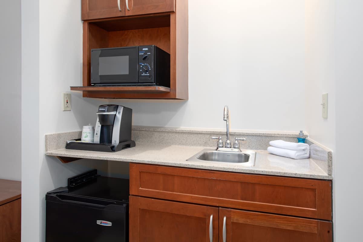 Una cocina compacta con microondas, cafetera, lavabo y armarios de madera.