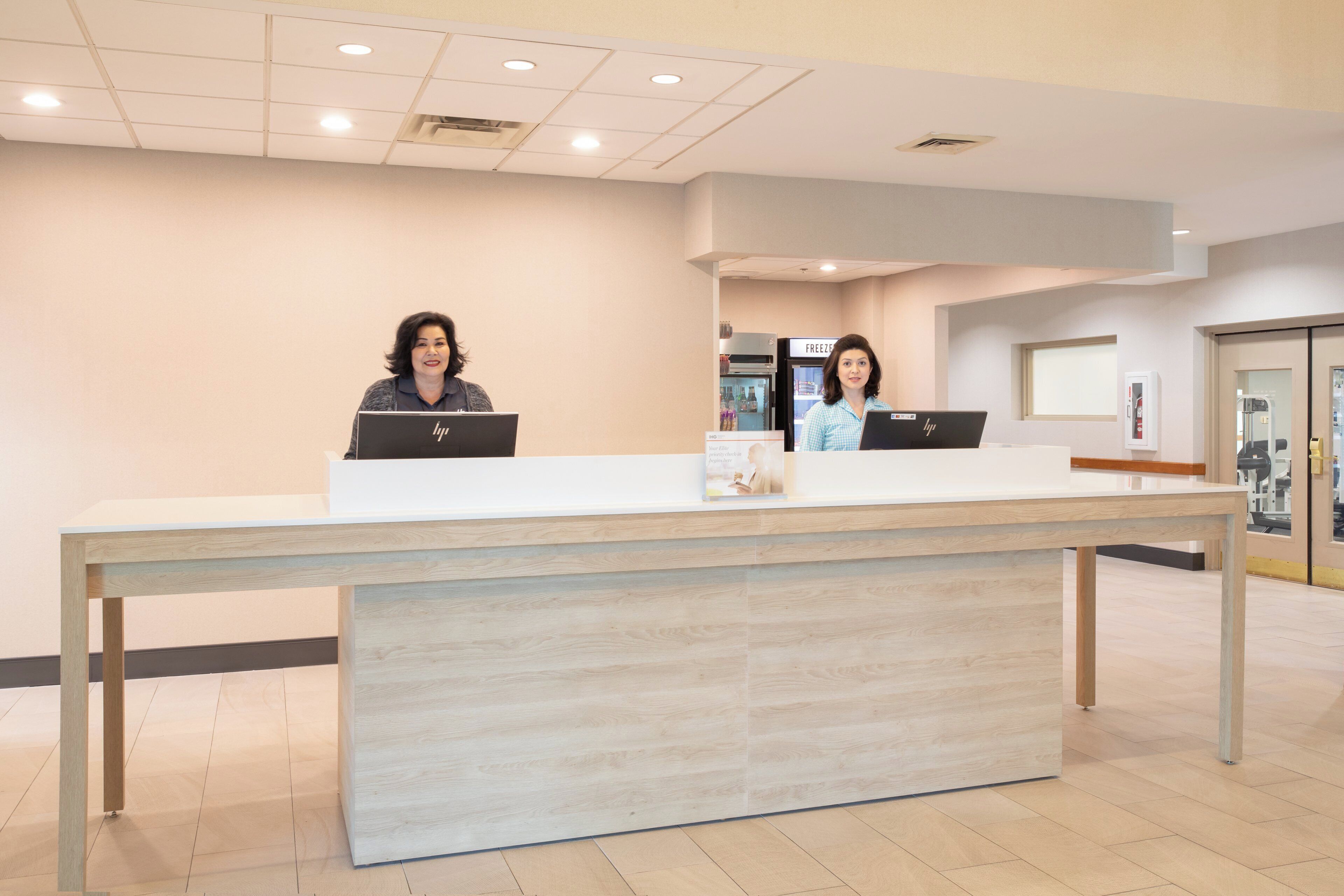 A reception desk with two individuals seated behind it, each using a laptop.
