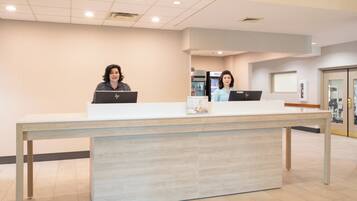 A reception desk with two individuals seated behind it, each using a laptop.