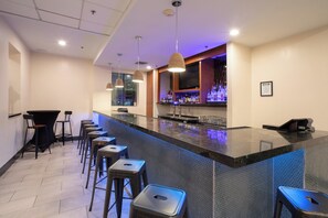 Una zona de bar con una barra larga, varios taburetes y una pantalla de televisión.