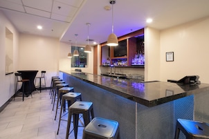 A bar area with a long counter, multiple stools, and a television screen.