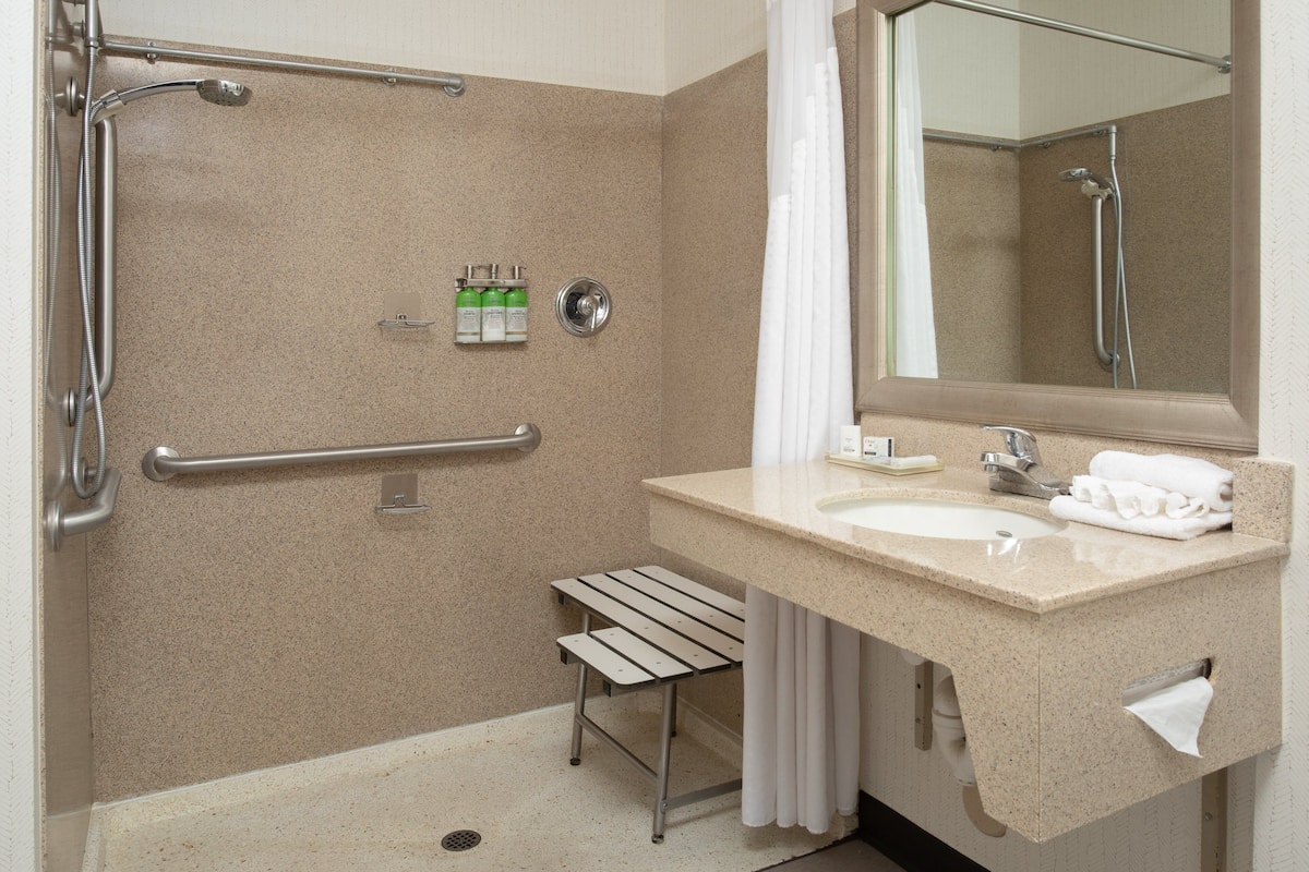 Baño con ducha, barra de apoyo, lavamanos y perchero.