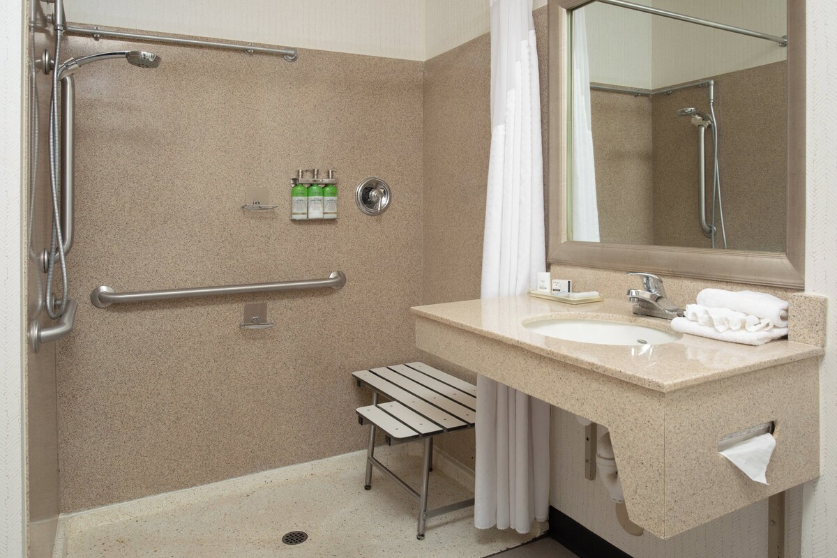 A bathroom with a shower, grab bar, sink, and towel rack.