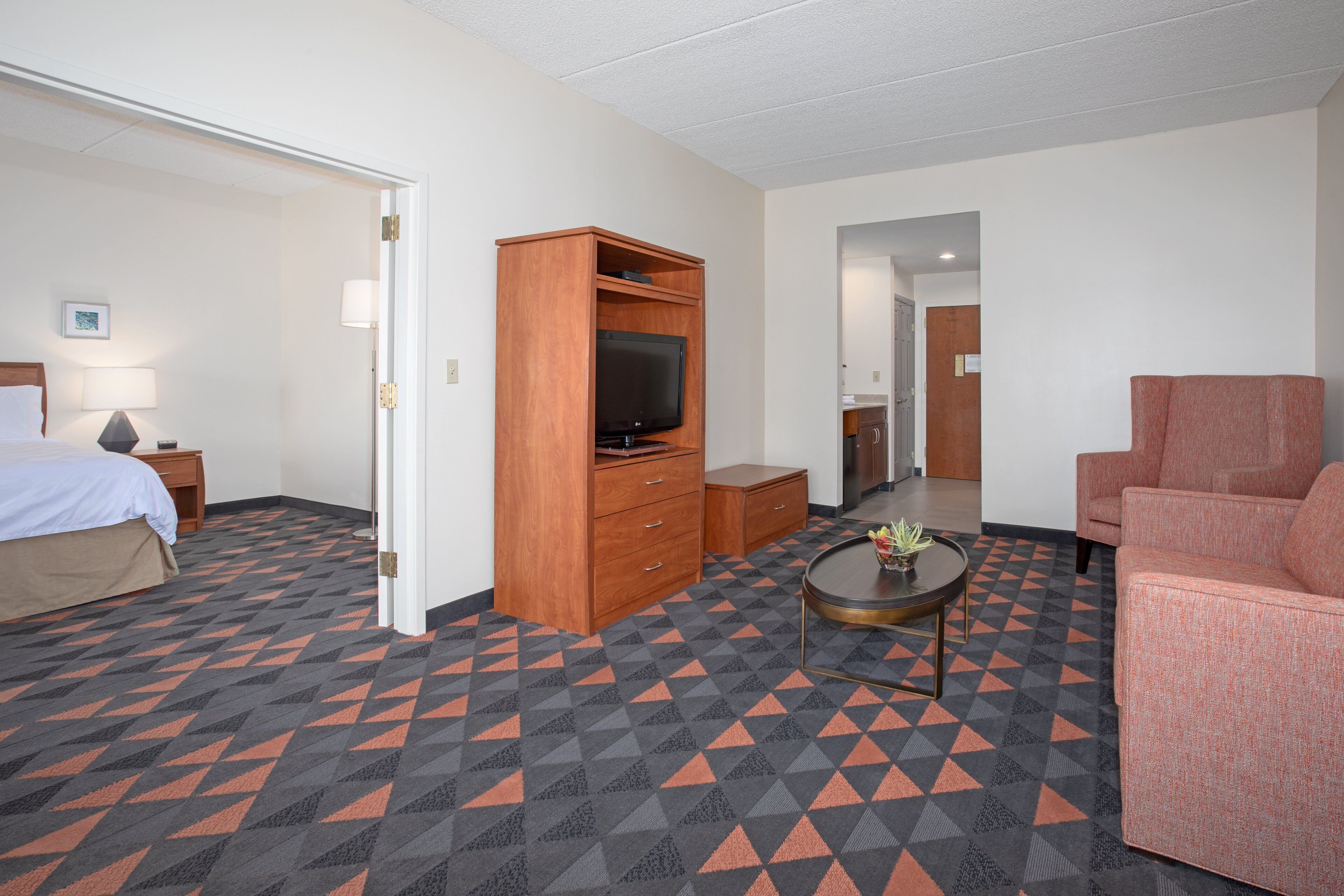 A hotel room with a bed, a TV, a sofa, a coffee table, and a dresser.