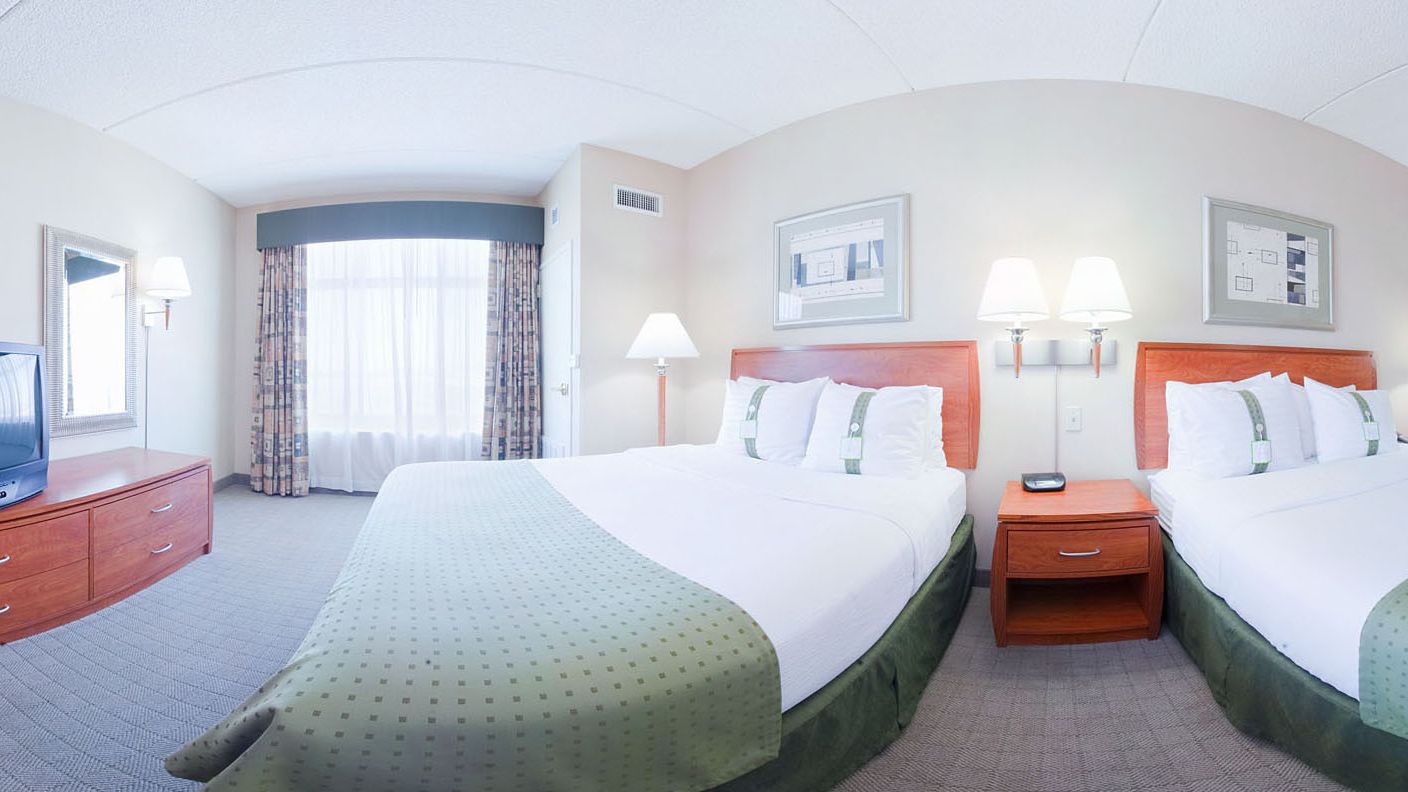 Habitación de hotel con dos camas, televisión, escritorio y ventana con cortinas.