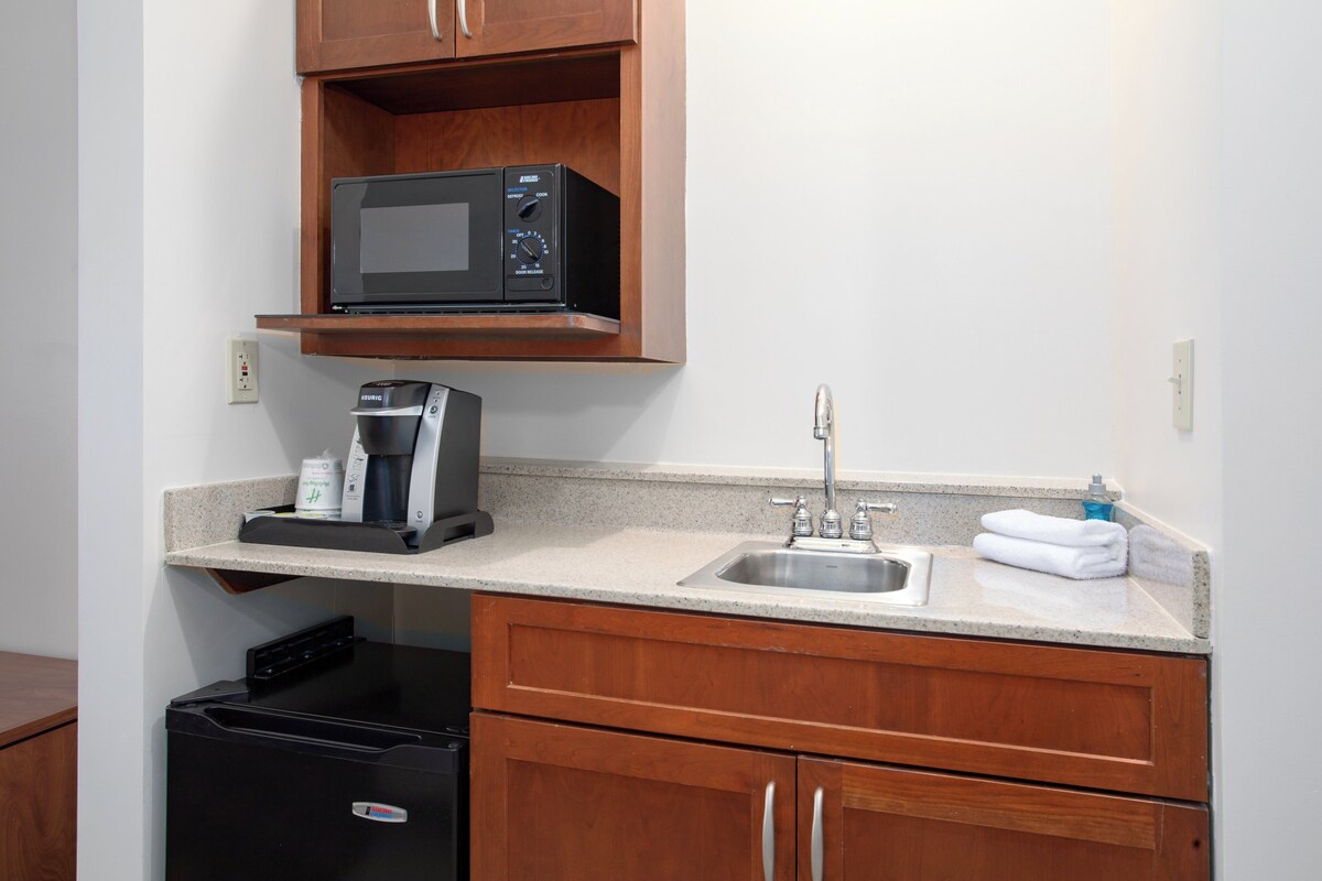 A compact kitchen with a microwave, coffee maker, sink, and wooden cabinets.