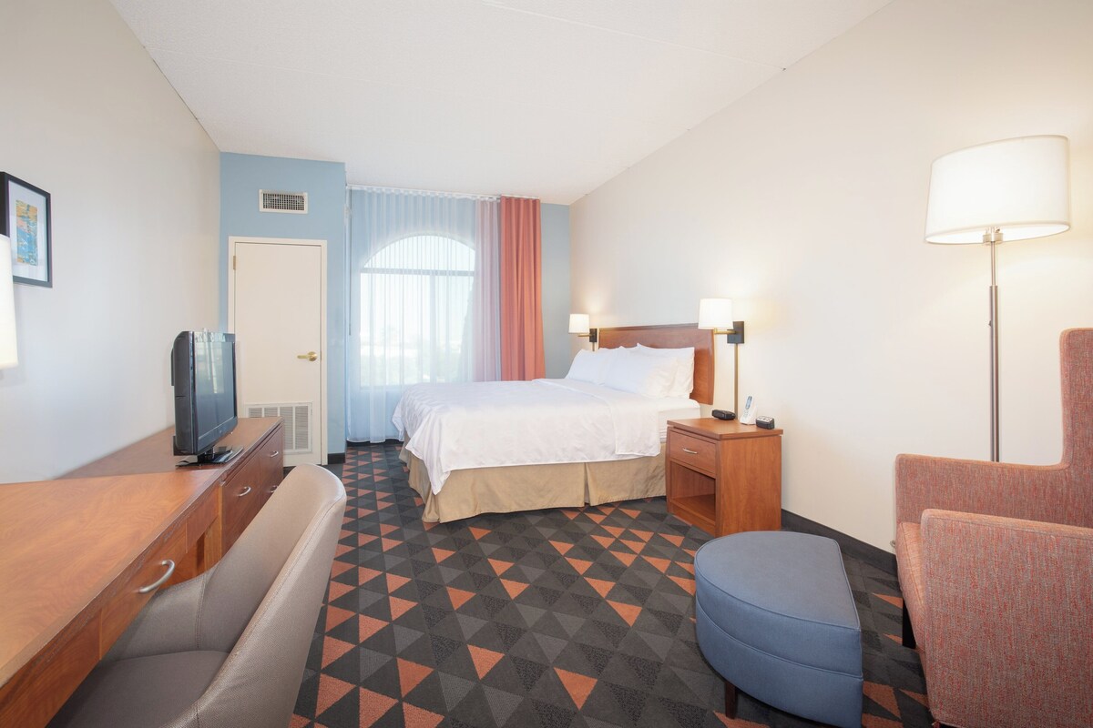 A hotel room with a bed, bedside tables, a desk, a television, and a patterned floor.