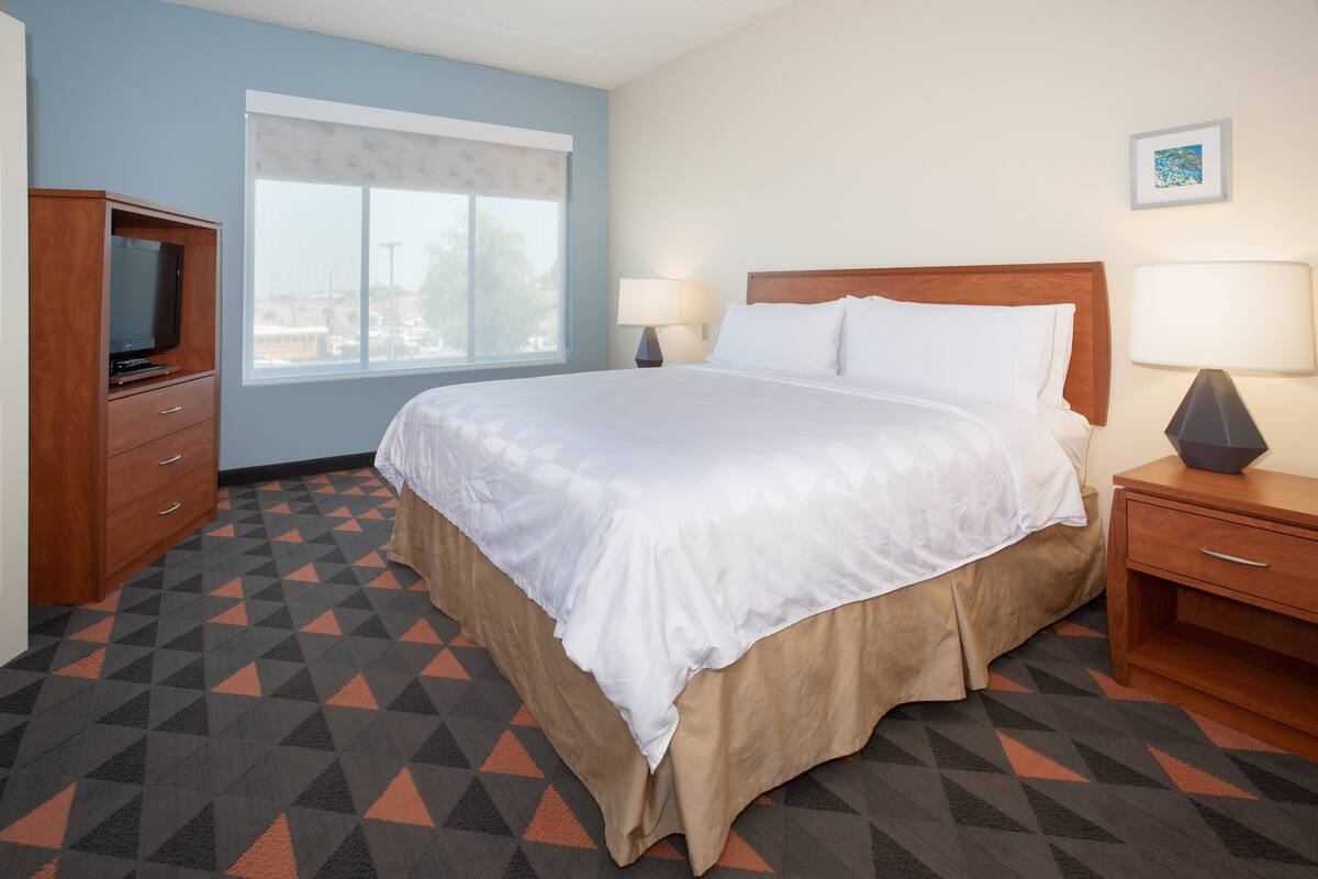 Una habitación de hotel con una cama grande, un televisor, una ventana y una lámpara.