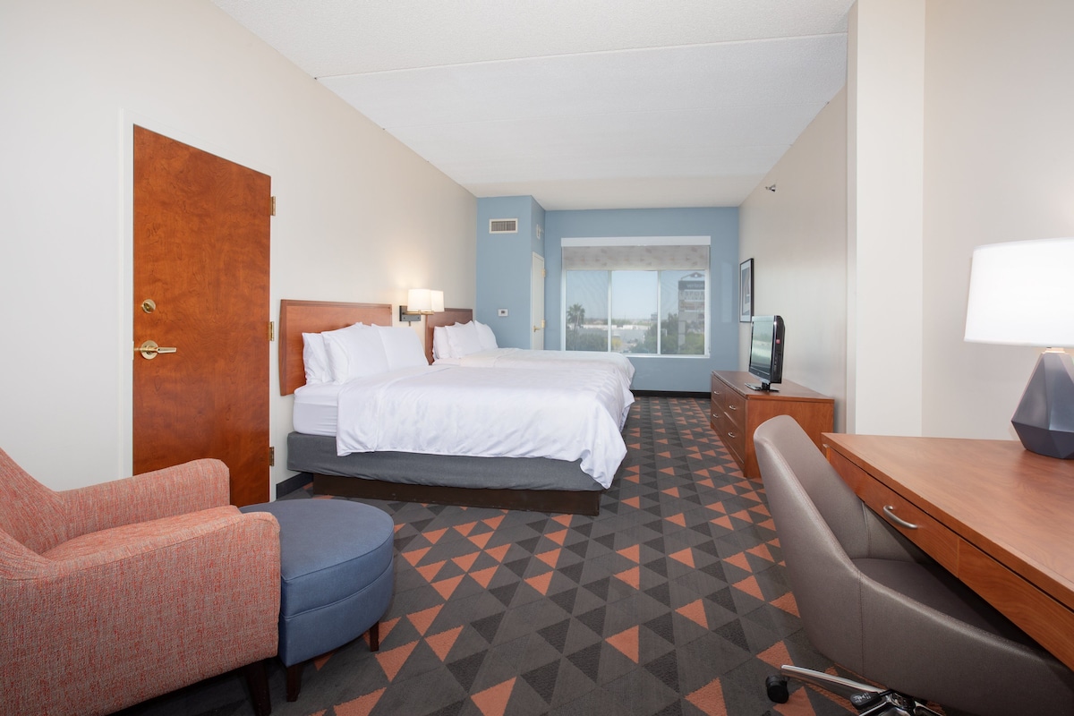 A hotel room with a bed, a desk, a chair, and a TV.