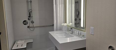 A bathroom with a shower, a sink, a mirror, and a towel rack.