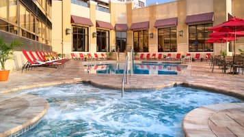 A hotel pool area with multiple lounge chairs and a hot tub.