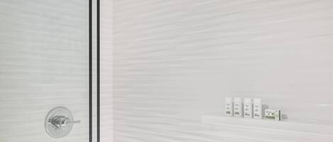 A modern bathroom with a glass shower enclosure, a built-in shelf with toiletries, and a sleek, minimalist design.