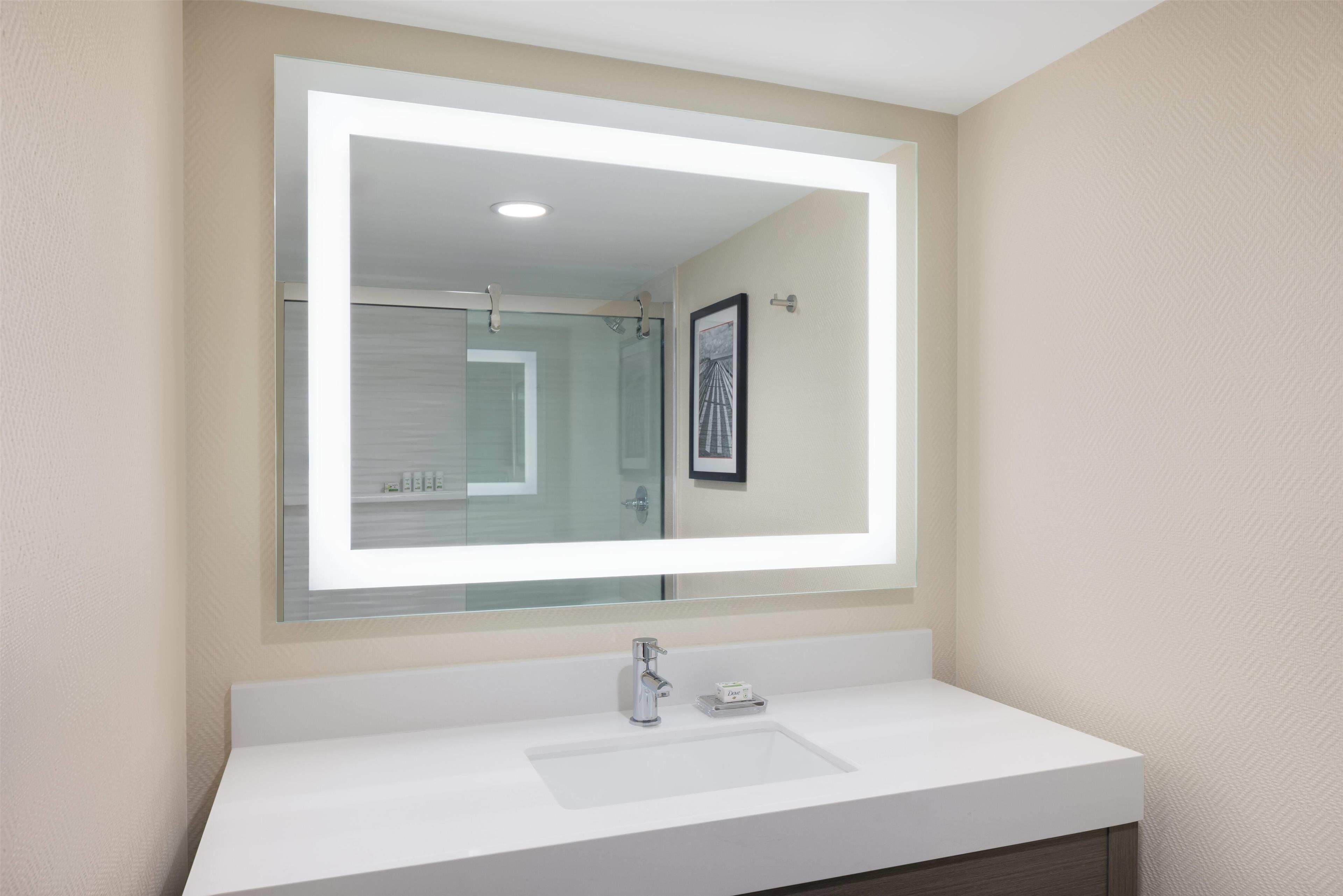 A modern bathroom with a large mirror, white sink, and a framed picture on the wall.