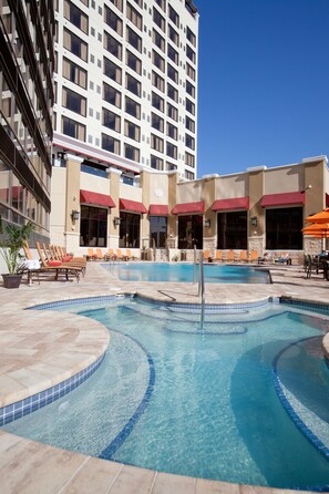 A hotel pool area with multiple lounge chairs, a hot tub, and a large building in the background. - Ramada Plaza Resort & Suites by Wyndham Orlando Intl Drive (Orlando)
