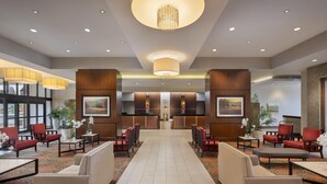 Eine Hotelhalle mit Empfangstresen, Sitzgelegenheiten und großen Fenstern.