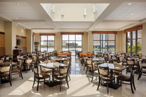 A spacious dining area with multiple tables and chairs, large windows with views of buildings, and a ceiling with recessed lighting. - Ramada Plaza Resort & Suites by Wyndham Orlando Intl Drive (Orlando)