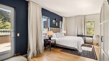 A bedroom with a bed, a desk, a chair, a window, and a view of a balcony.