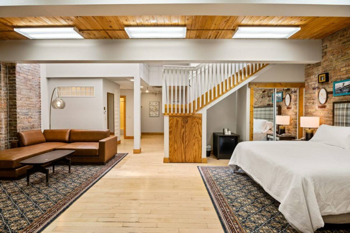 Amplia sala de estar con techo de madera, una escalera, un sofá, una cama y un tapete estampado.